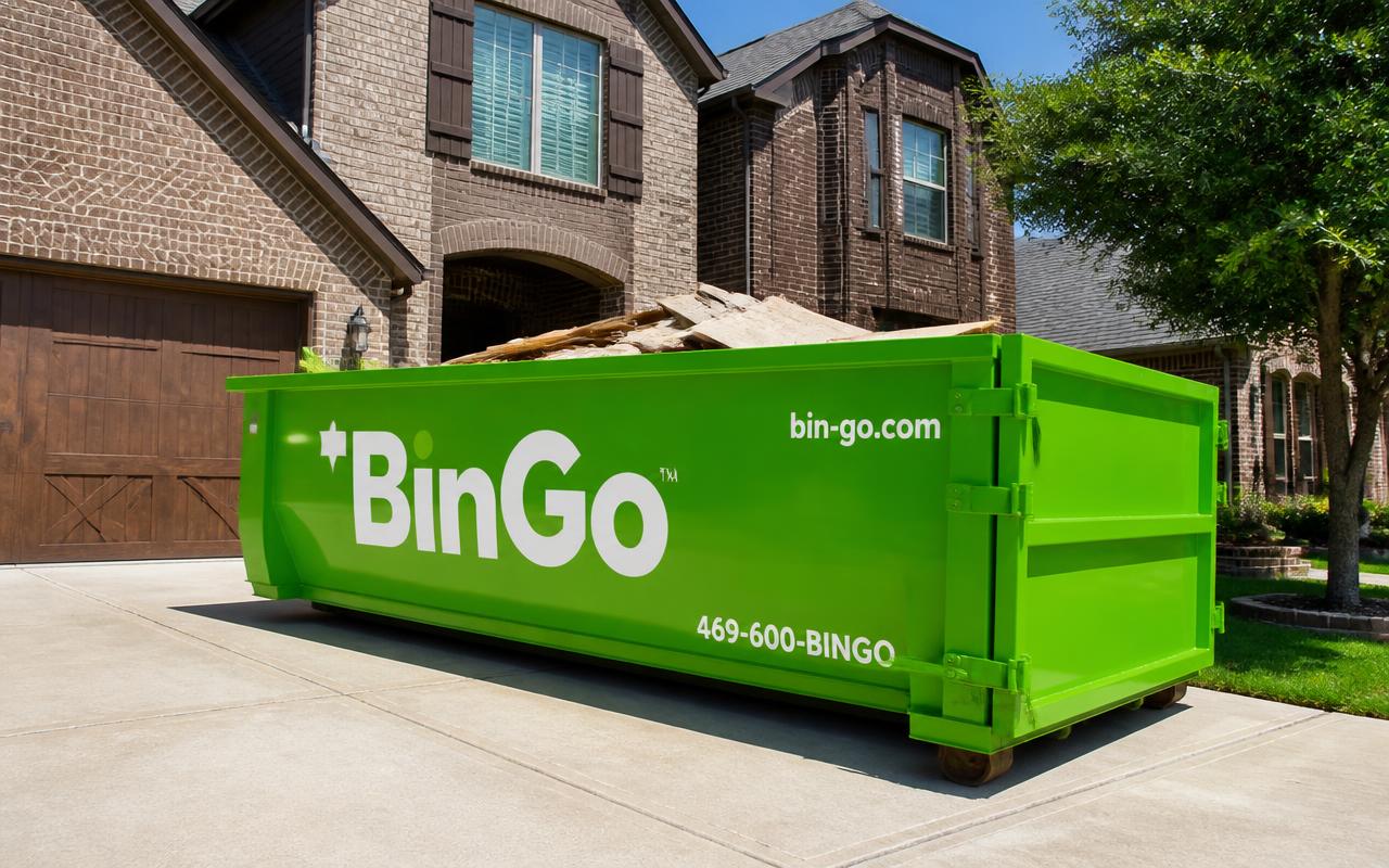 Green BinGo roll-off dumpster filled with remodel lumber on a brick home driveway in Sachse, TX